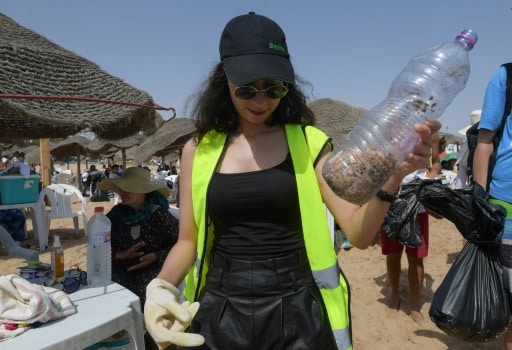 Une volontaire de l'association Tounes Clean-Up, qui organise des opérations de nettoyage toute l'année, ramasse des mégots de cigarettes sur la plage de La Marsa, près de Tunis, le 14 juillet 2019 © AFP FETHI BELAID
